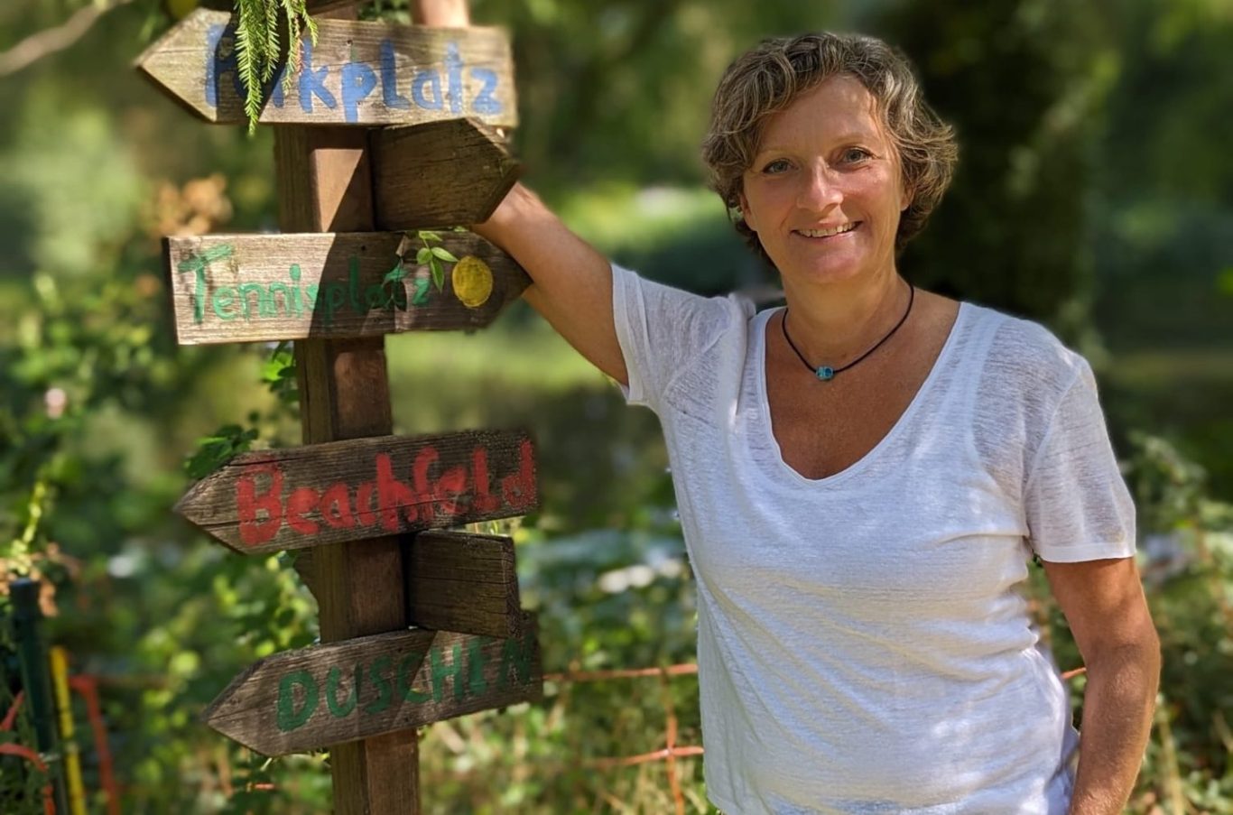 Eine Frau steht neben einem Schilderbaum mit Richtungshinweisen in einer grünen Umgebung.